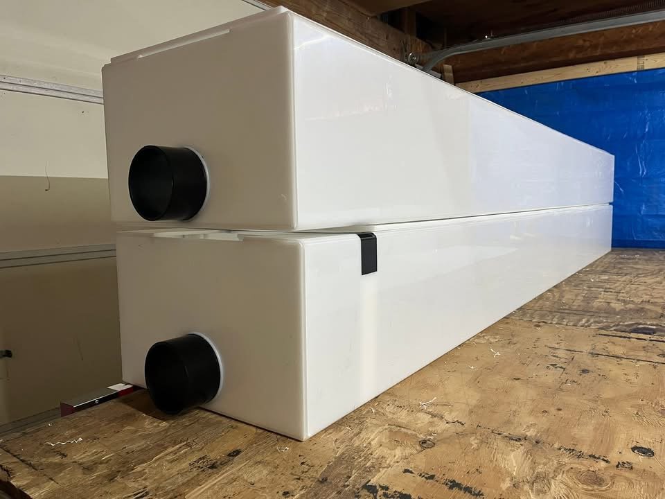Two custom white HDPE drain troughs with black discharge ports, stacked in the shop